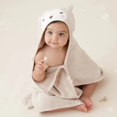 A baby sitting with bath products with a cream colored animal towel wrapped around them.