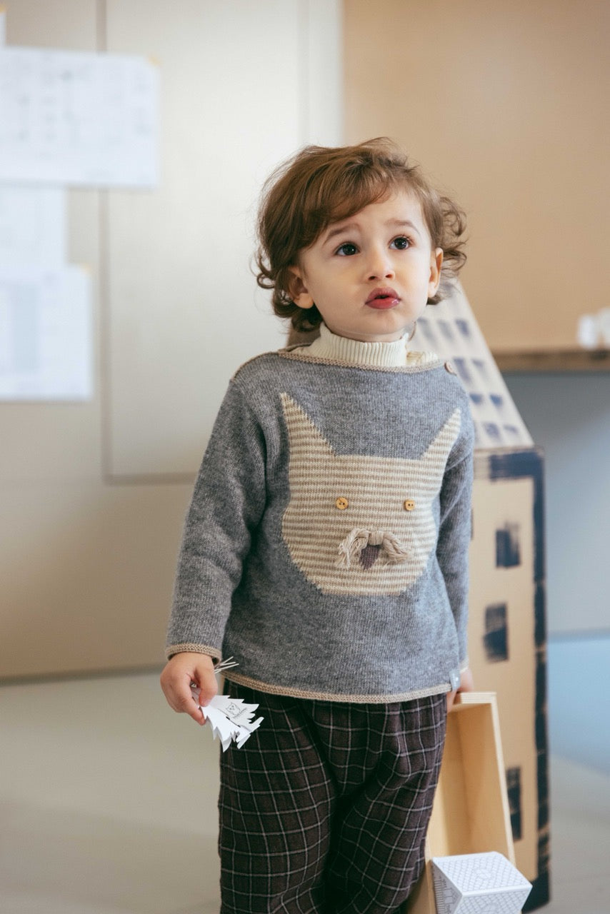 Child wearing a gray sweater with a cat design in a room with a lamp and box in the background