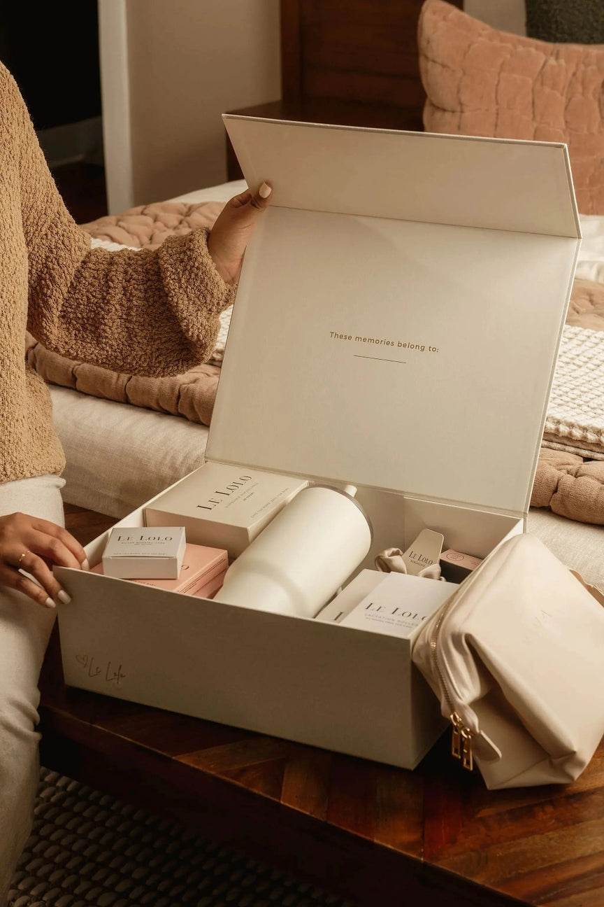 Person opening a white box containing a skincare product on a wooden table.