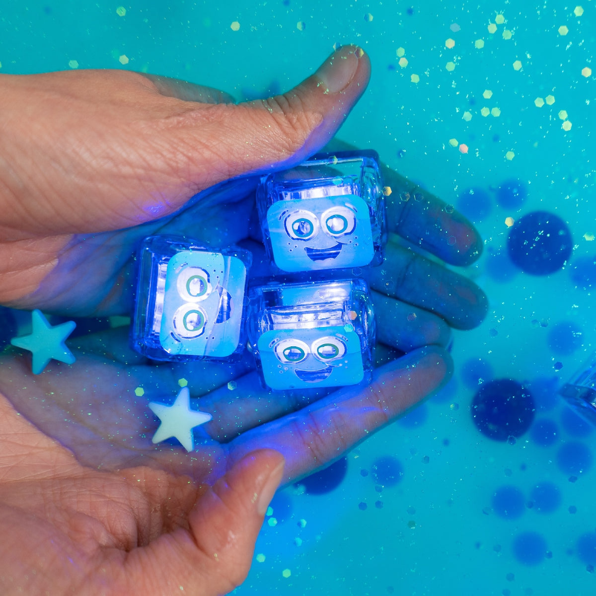 Hand holding blue LED dice with robot faces against a blue glittery background