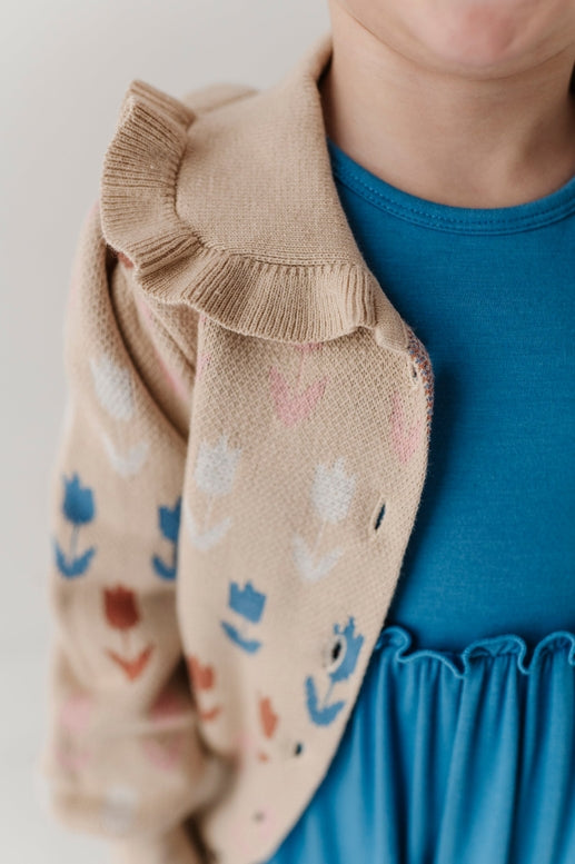 Close-up of a child wearing a beige cardigan with floral patterns and a blue dress.