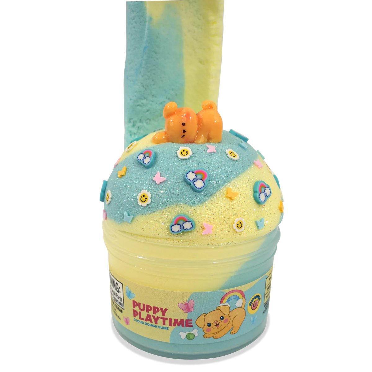A novelty slime container labeled 'PUPPY PLAYTIME' filled with two-toned pastel blue and yellow slime, topped with a small orange bear figure and decorated with colorful flower and rainbow charms, on a plain white background.