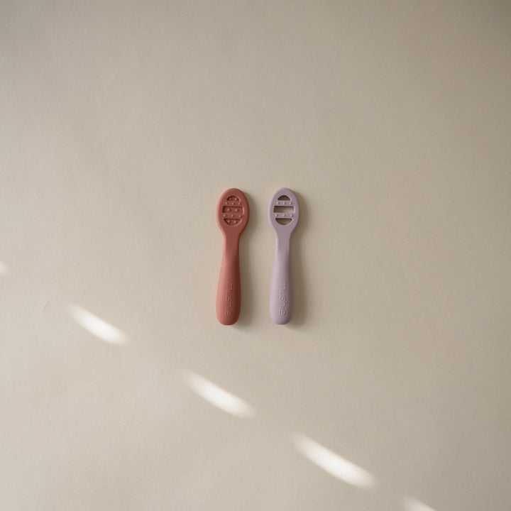 Two baby rattles, one red and one purple, on a beige surface.