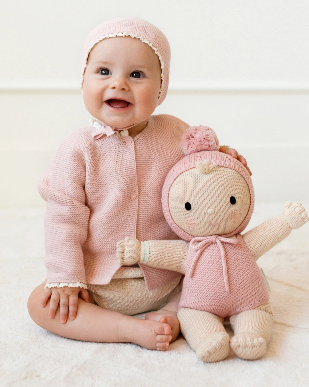 Baby in pink outfit with matching doll on a white background