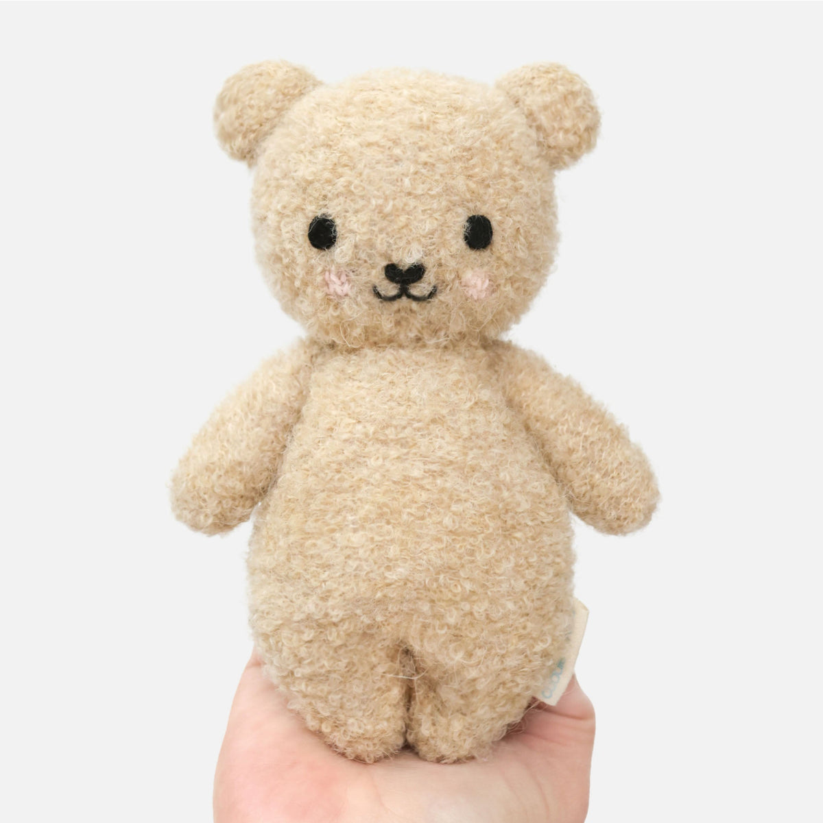 Small beige teddy bear held in a hand against a white background