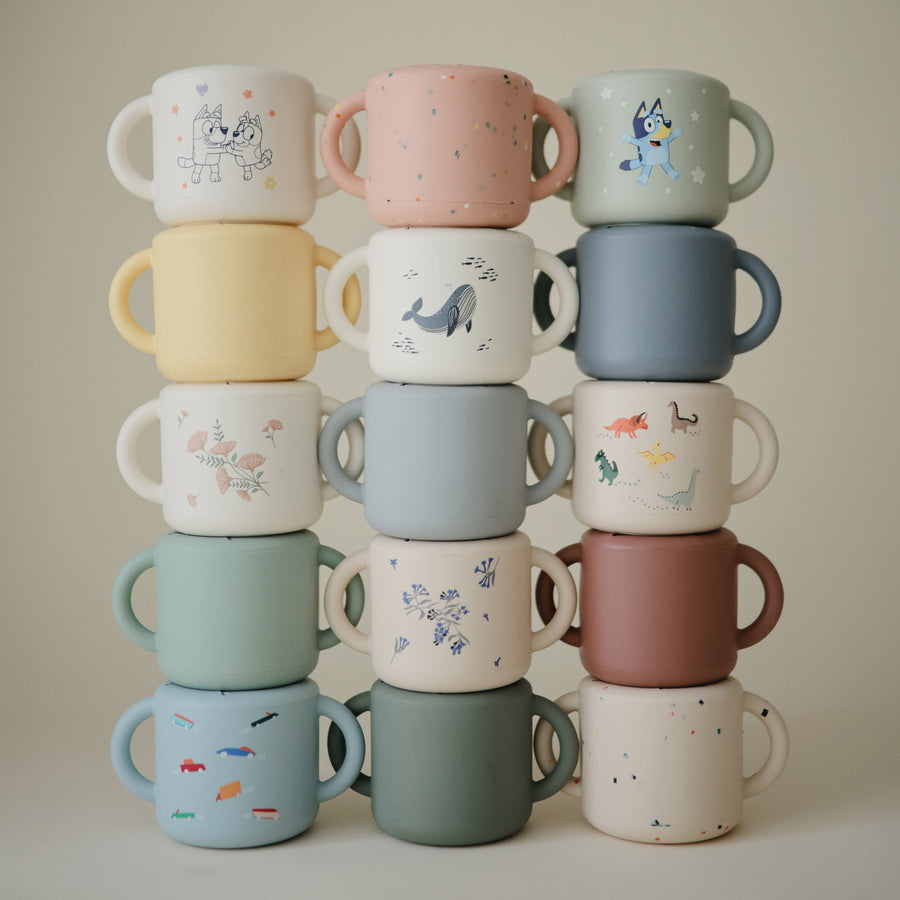 Stack of colorful children's mugs with various designs on a neutral background