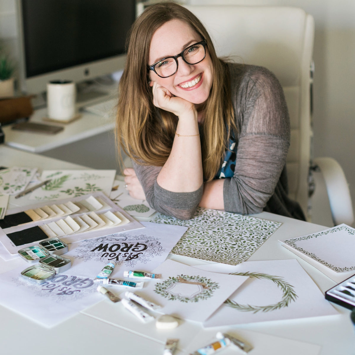 Woman sitting at a desk with design materials and a computer in the background