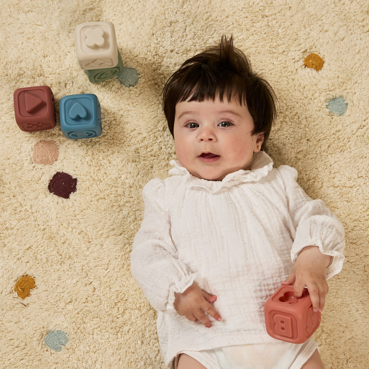 Baby lying on a carpet with colorful blocks around