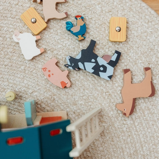 An overhead, bird's-eye view of the Wooden Big Red Barn Playset by Mentari components laid out on a textured surface, including seven wooden animal figures—a cow, horse, pig, sheep, goat, chicken, and rooster—alongside a blue ladder, a small stool, and a piece of fencing.