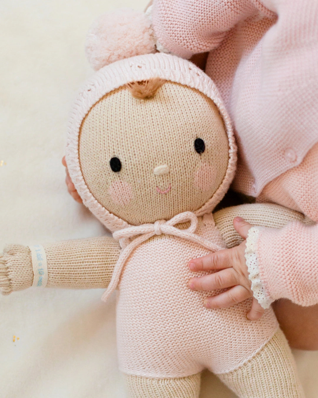 Knitted doll with a pink outfit held by a person against a light background