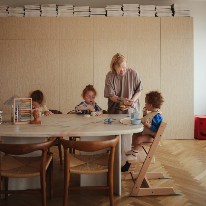 Woman with three children at a table in a room with wooden furniture and light-colored walls.