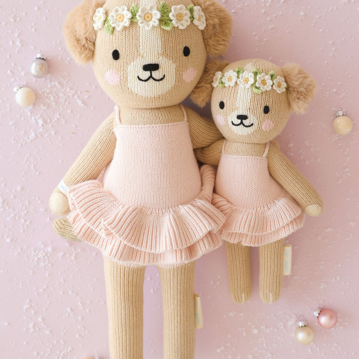 Two teddy bears in ballet costumes with flower crowns on a pink background