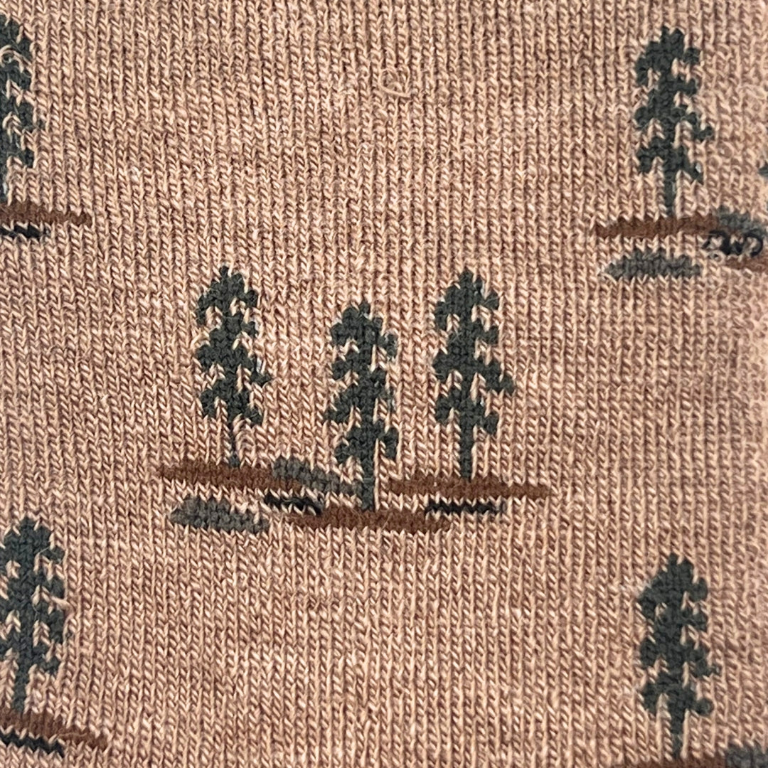 Close-up of a woven fabric with a repeating pattern of dark green pine trees on brown ground over a warm tan background.