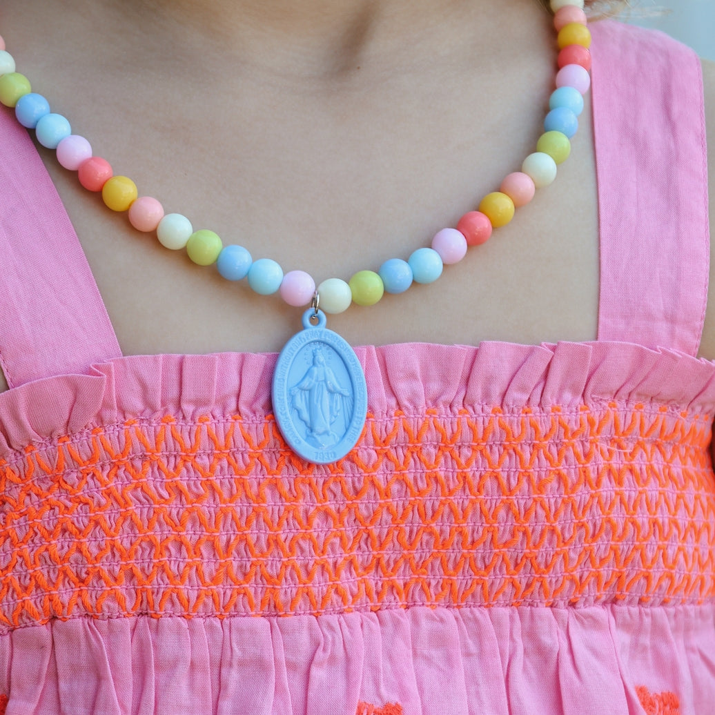 Child wearing a colorful beaded necklace with a blue pendant on a pink dress.