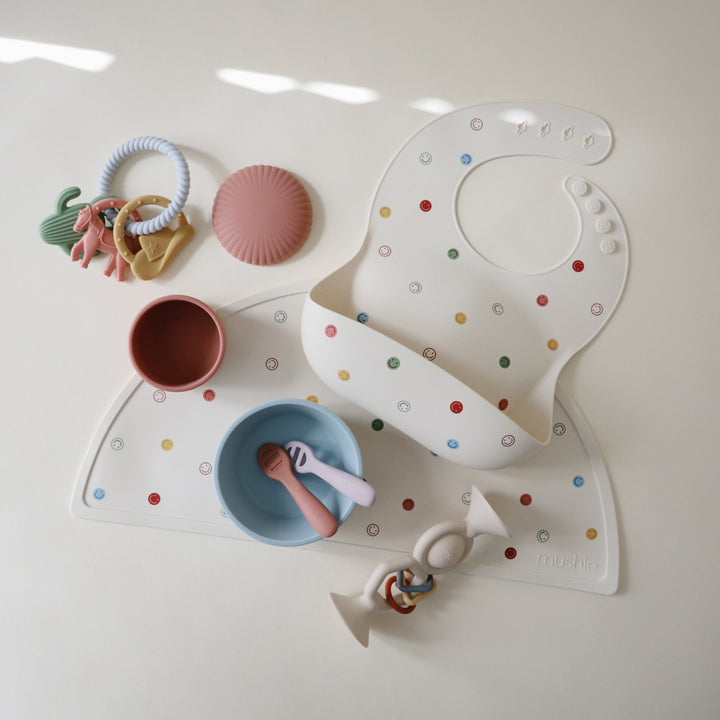 Baby feeding set with bib, bowl, spoon, and toys on a white surface