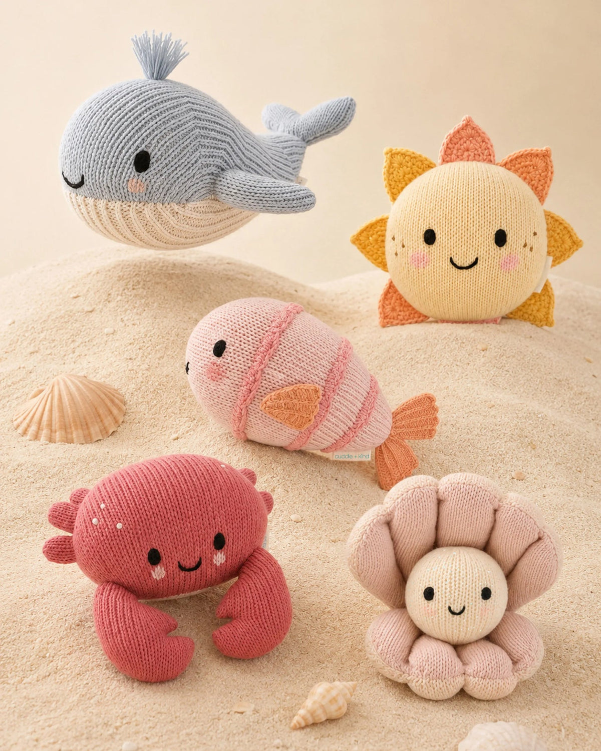 Set of knitted sea-themed toys including a whale, fish, crab, and starfish on a sandy background.