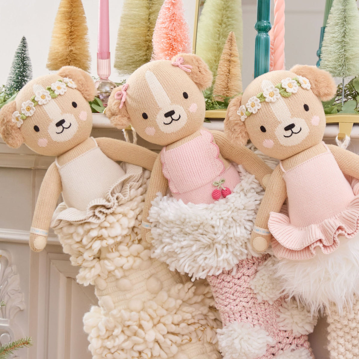 Three teddy bears in dresses sitting on a textured surface with decorative trees in the background.
