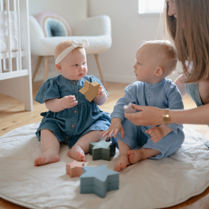 Two children playing with star-shaped blocks on a bed in a nursery.