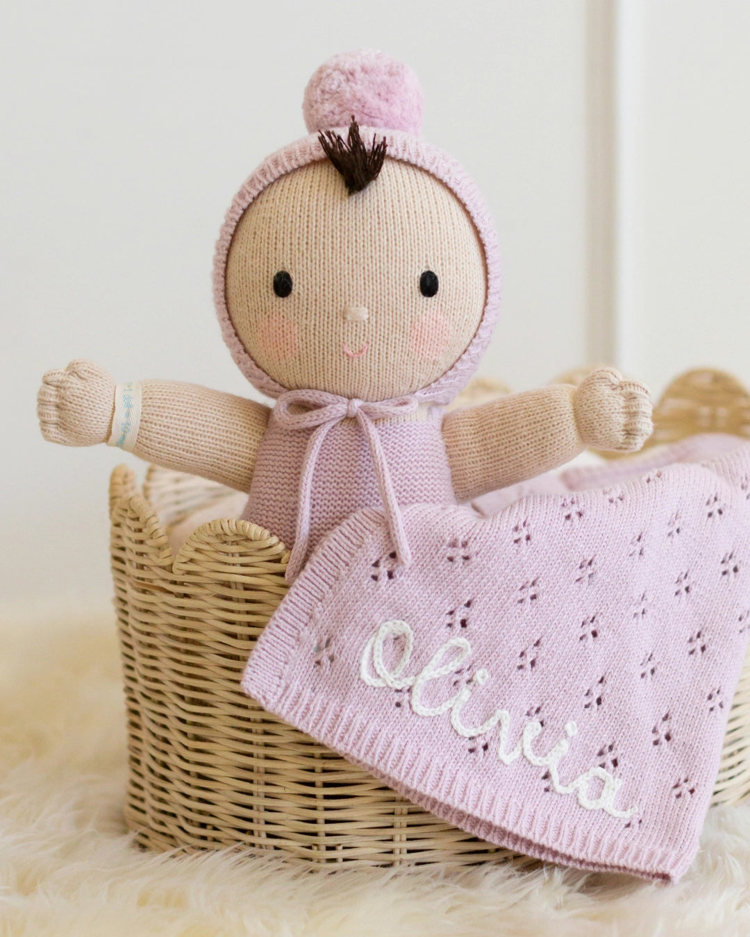 Knitted doll with pink outfit and blanket named 'Olivia' in a basket
