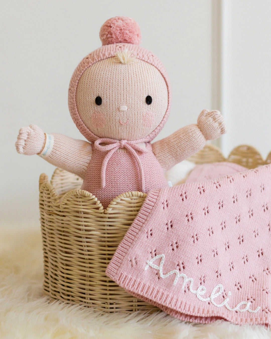 Knitted doll with pink outfit and matching blanket named 'Amelia' in a wicker basket.