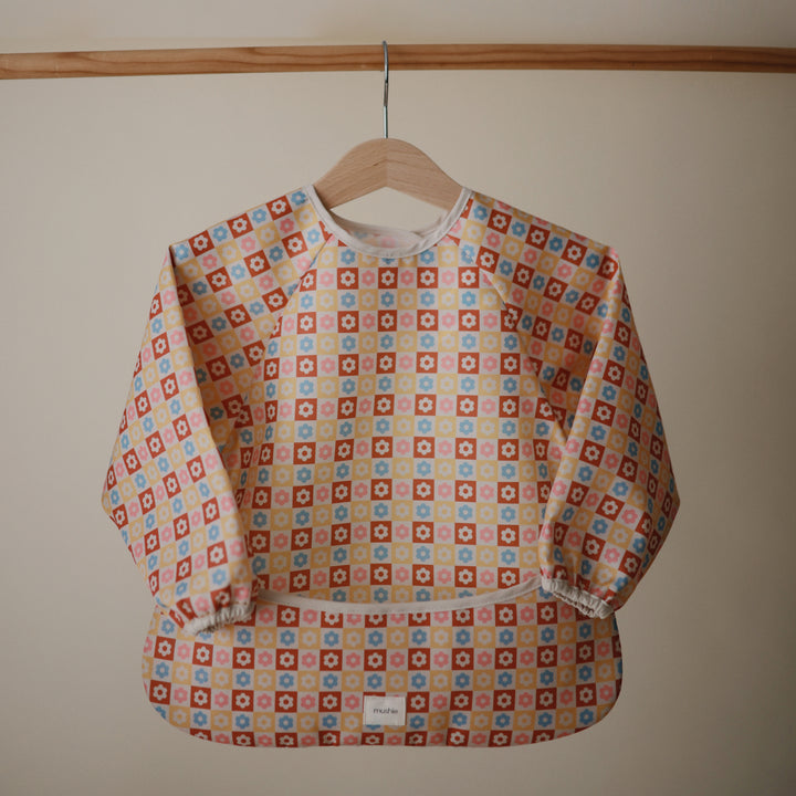 Patterned bib on a wooden hanger against a beige wall