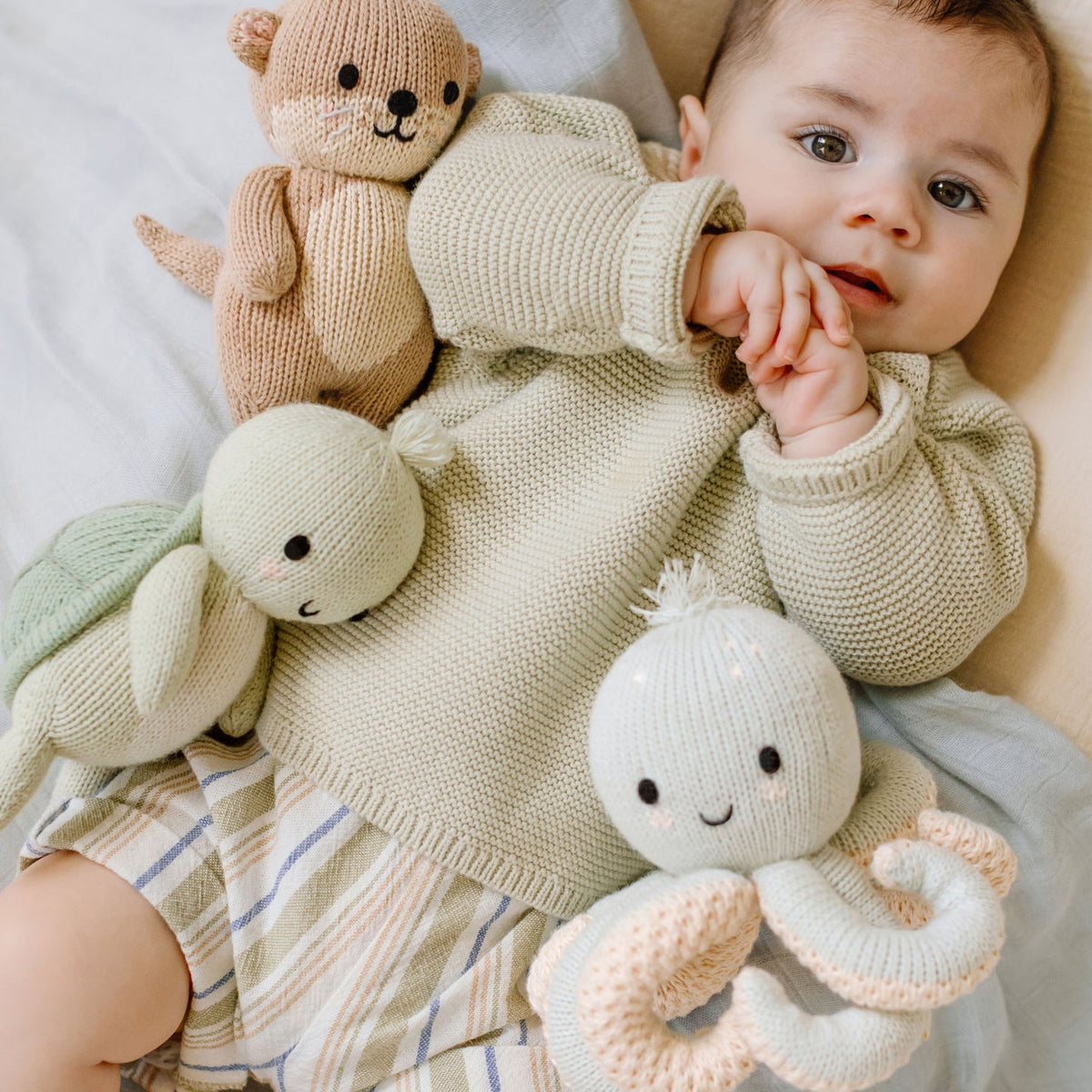 Baby with a knitted teddy bear and octopus on a soft surface