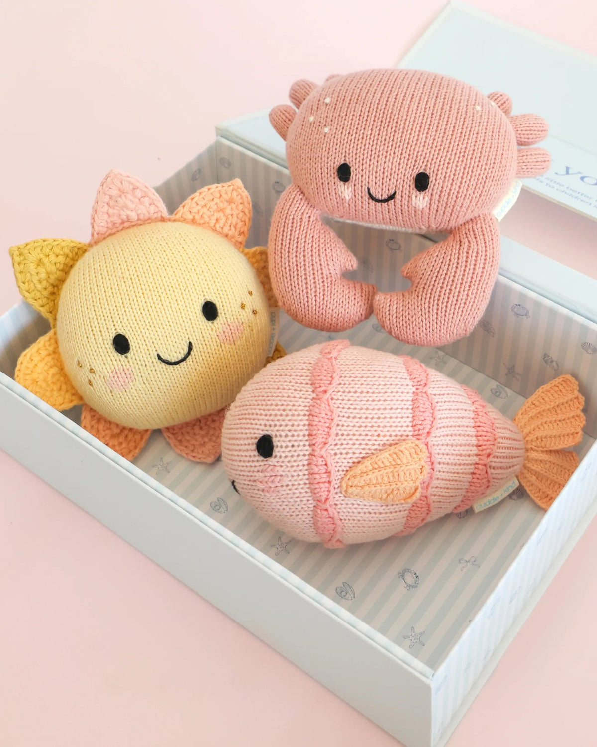 Three knitted toys shaped like a sun, a crab, and a fish on a pink surface.