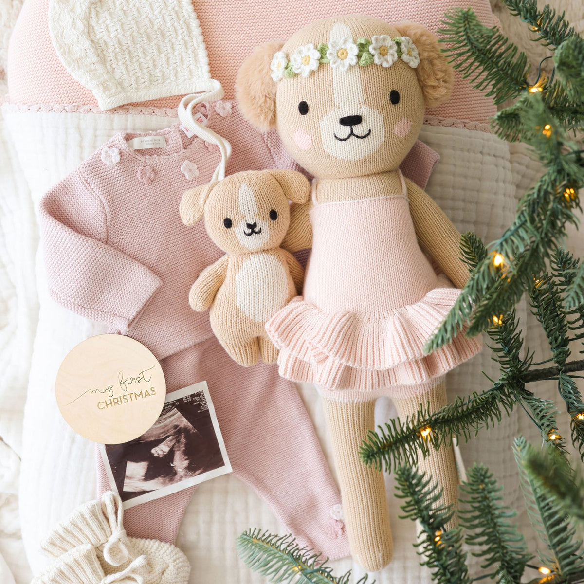 Two teddy bears in pink outfits with a Christmas tree and decorations.