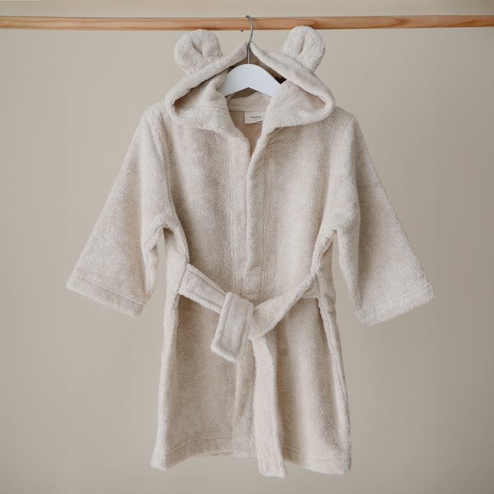 Beige children's robe with bear ears on a hanger against a beige wall