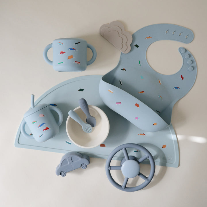 Children's tableware set with blue car-shaped tray, bowl, cup, and spoon on a light background