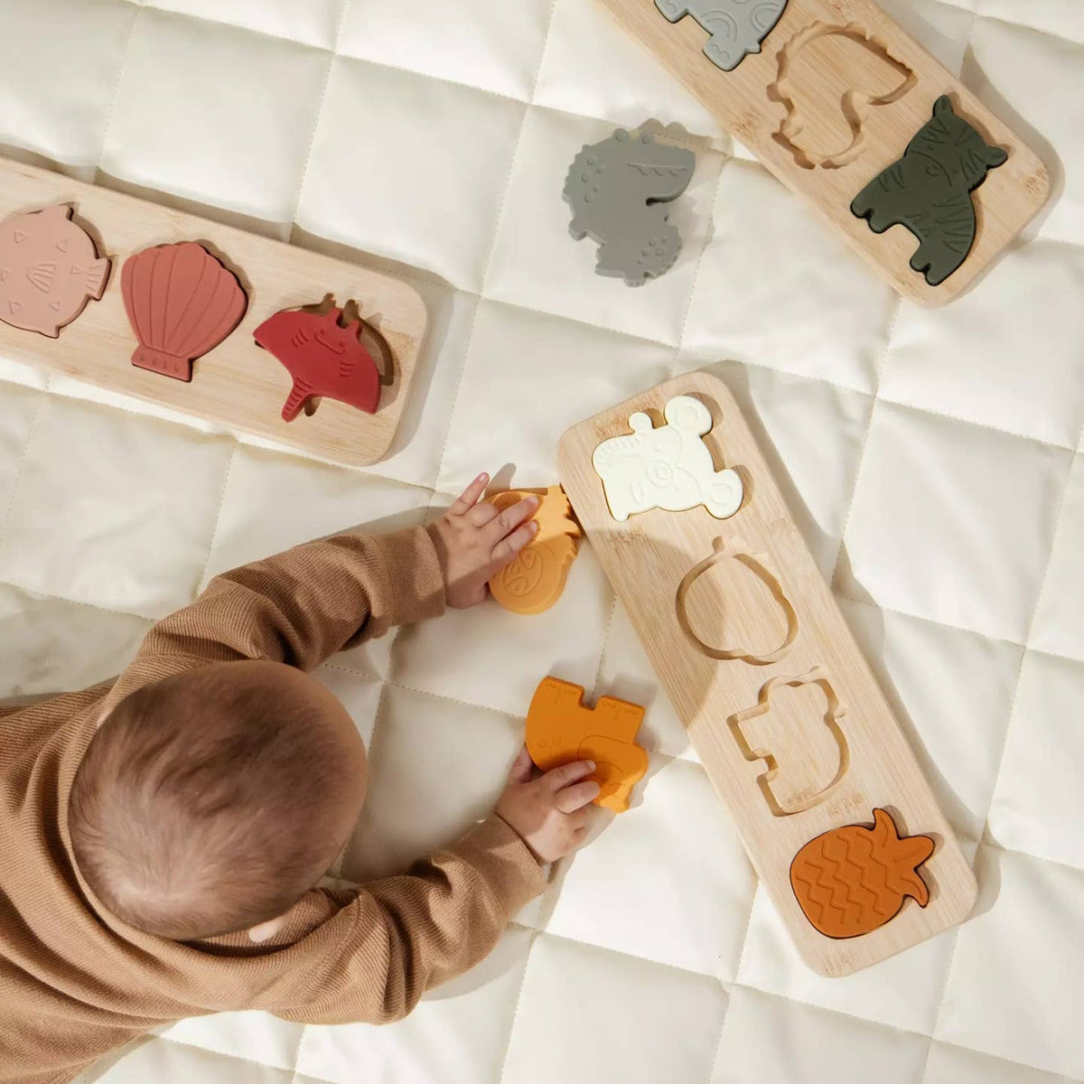 Child playing with wooden shape sorting toys on a white blanket
