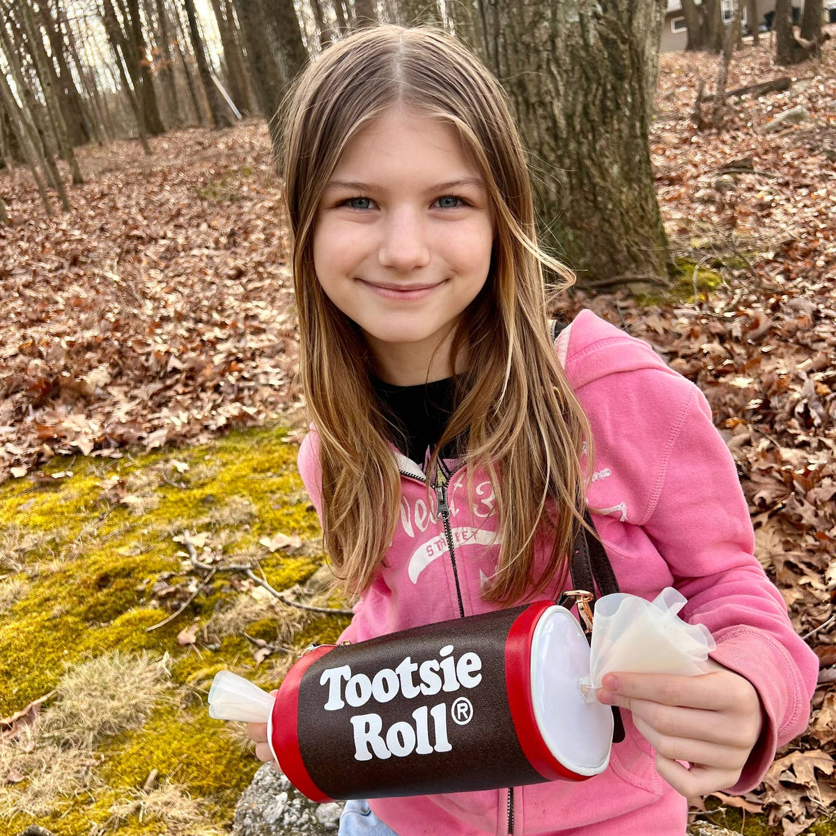 Young girl holding a Tootsie Roll candy container in a forest setting