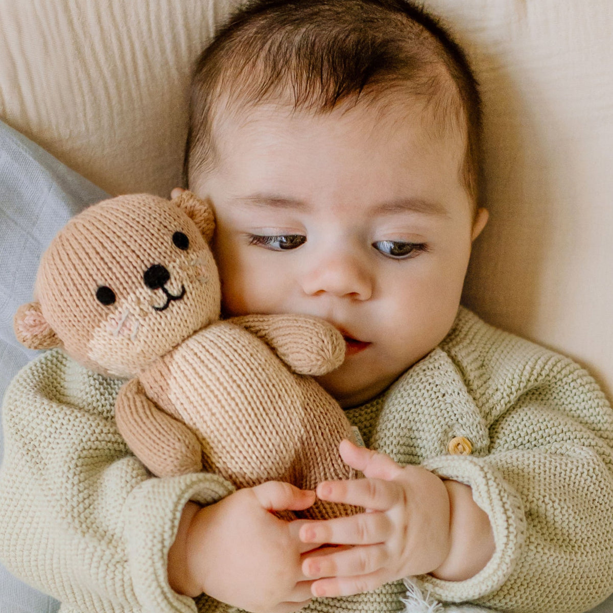 Baby holding a knitted teddy bear on a soft surface