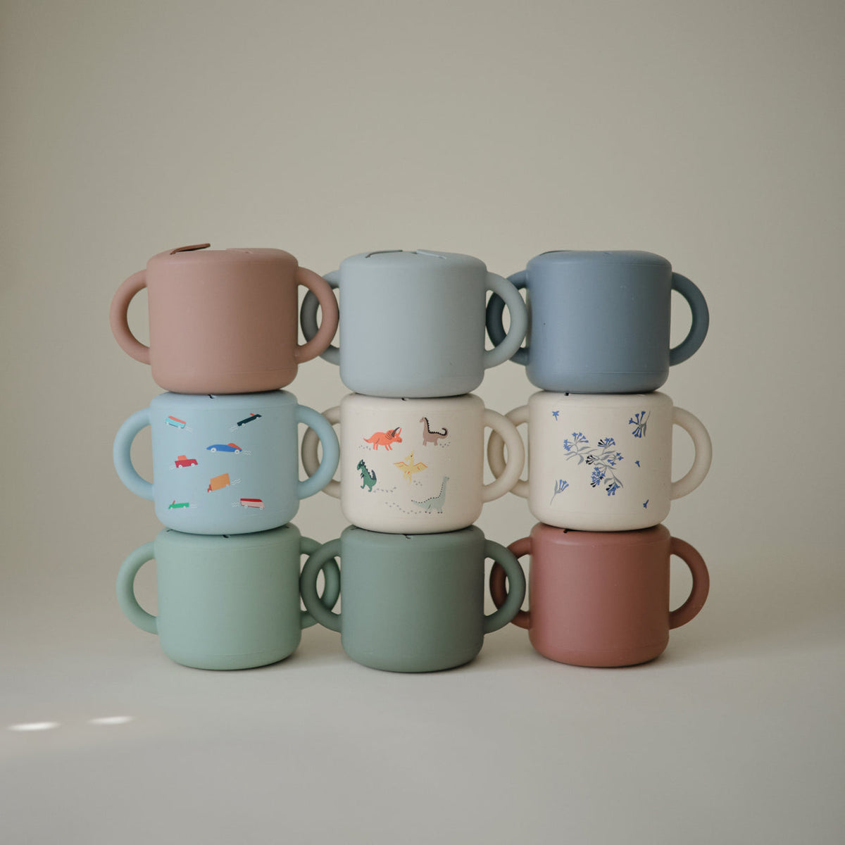 Stack of colorful ceramic cups with handles on a neutral background
