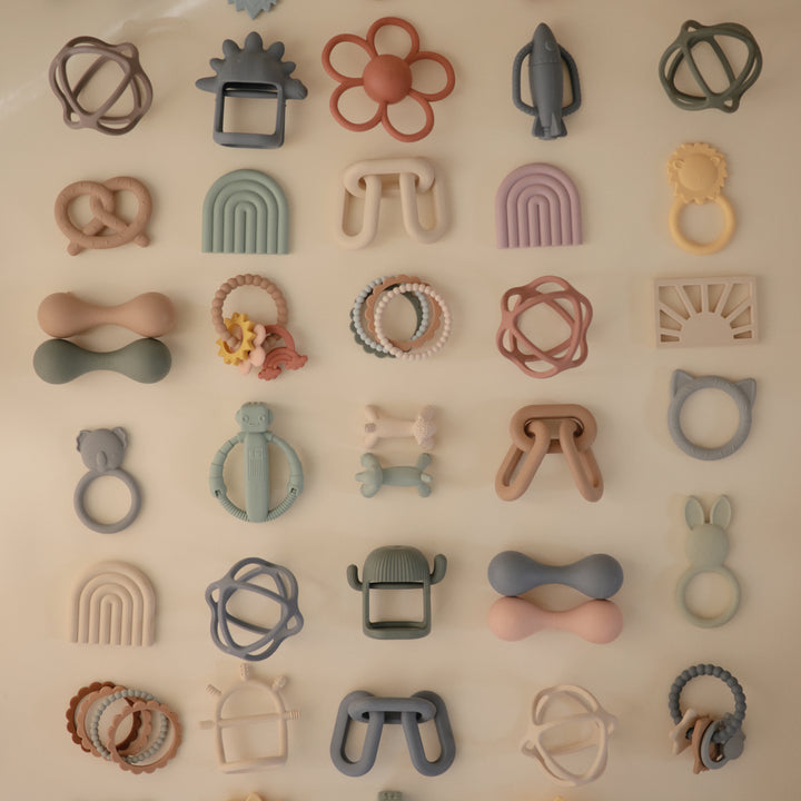 Collection of various silicone teething rings in different shapes and colors on a beige background