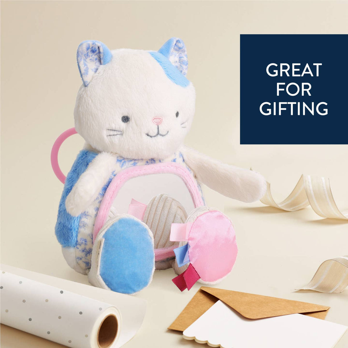 Plush toy with blue and pink accents on a beige background with gift-wrapping materials.