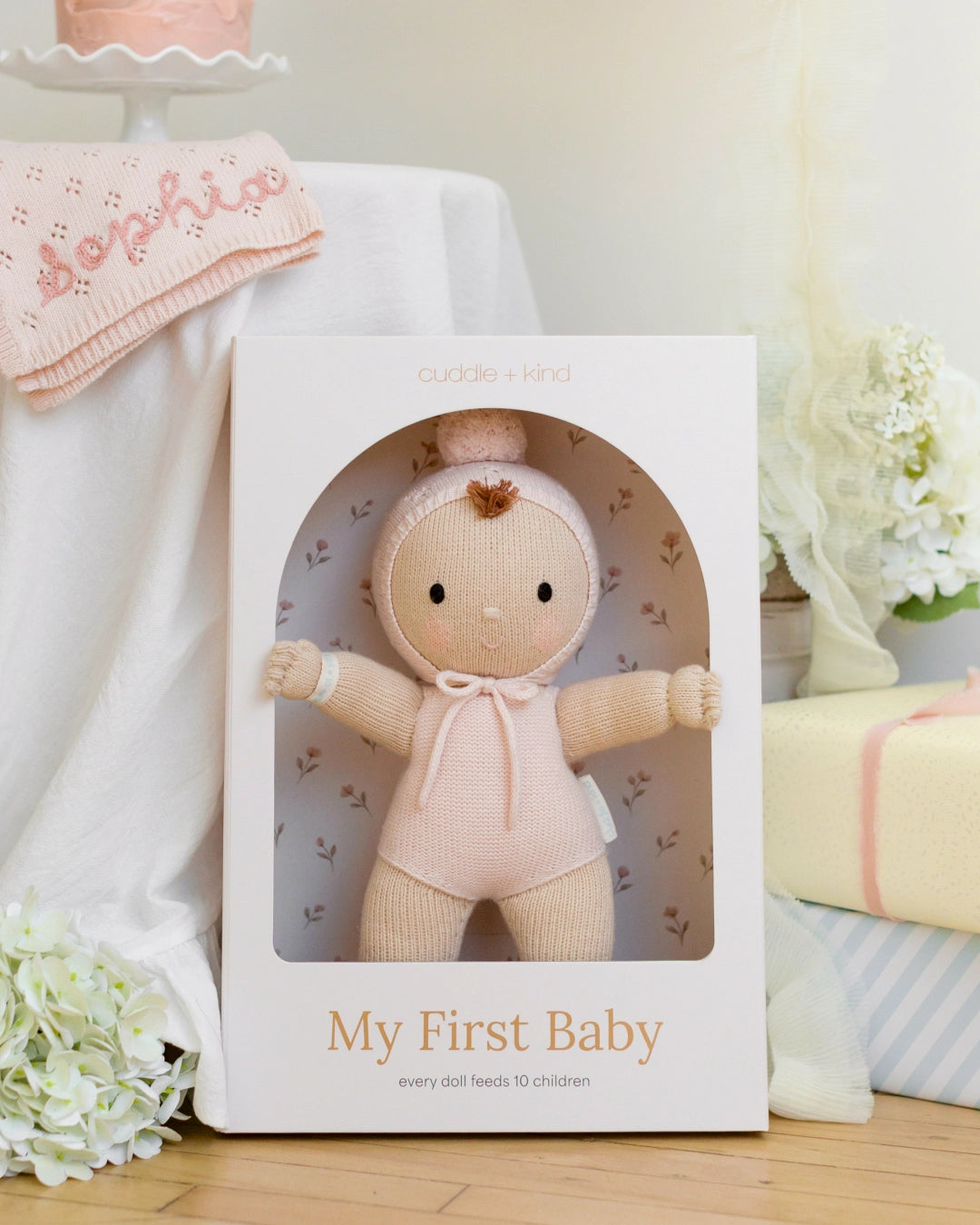 Cuddle + Kind doll in packaging with 'My First Baby' text on a pink background