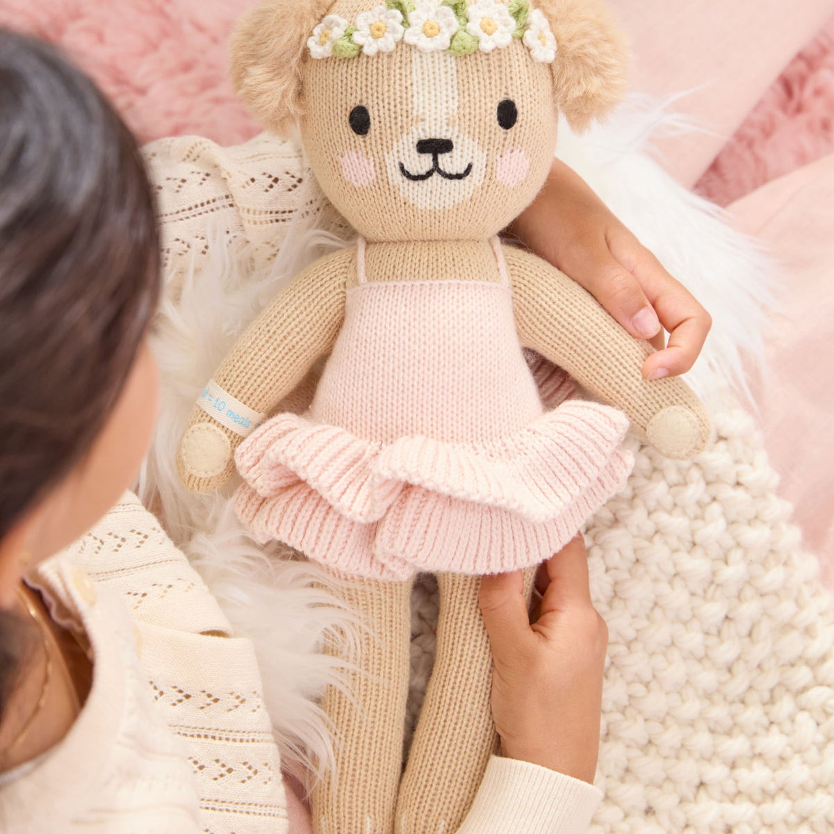 Knitted teddy bear in a pink dress held by a person against a soft pink background