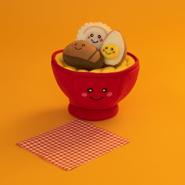 Red bowl with plush toys resembling a bun, rice cake, and egg on an orange background