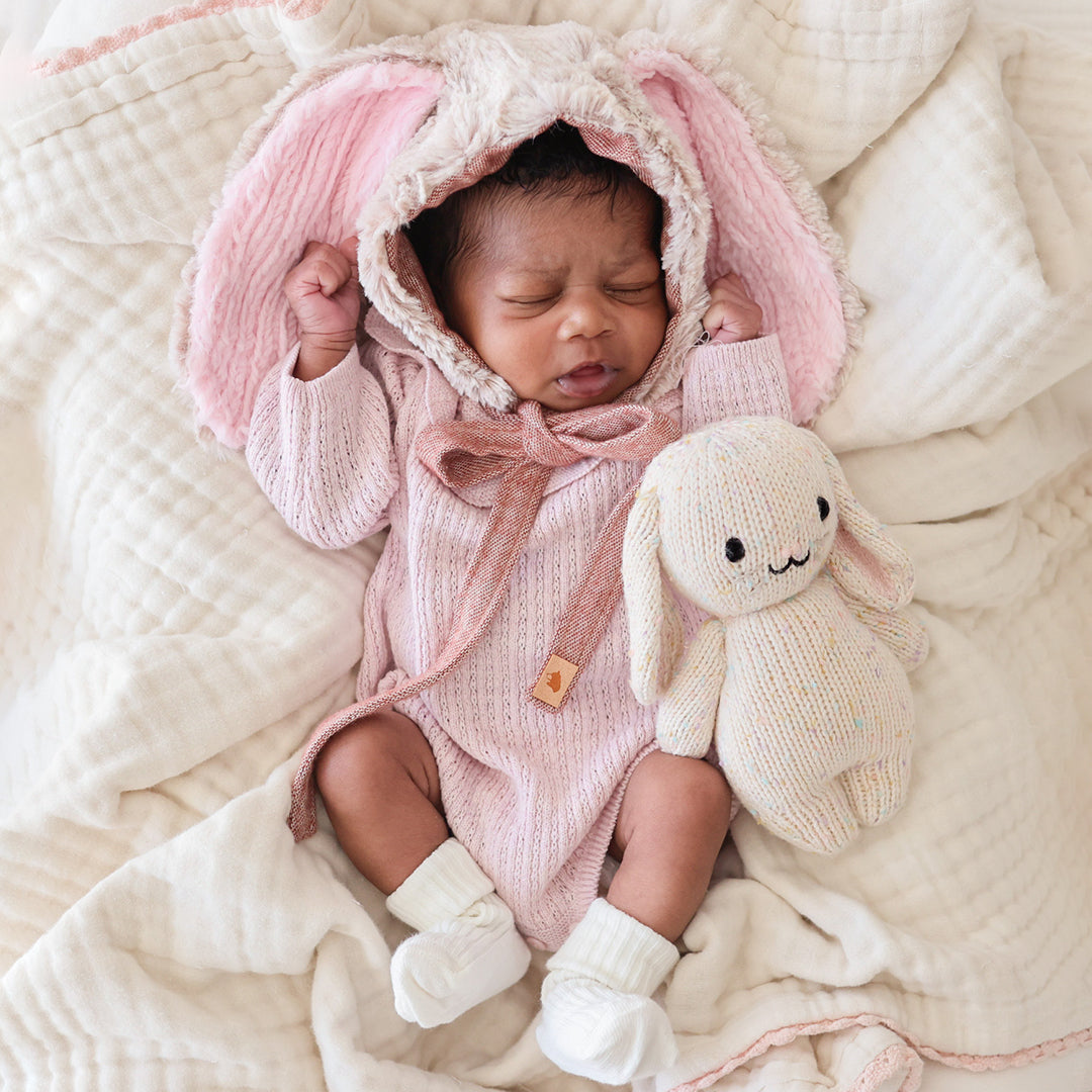 Newborn baby in a pink bunny outfit with a plush toy on a soft blanket