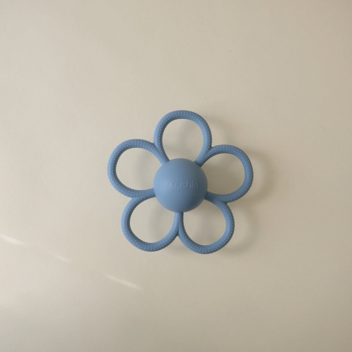 Blue flower-shaped teething ring on a beige background