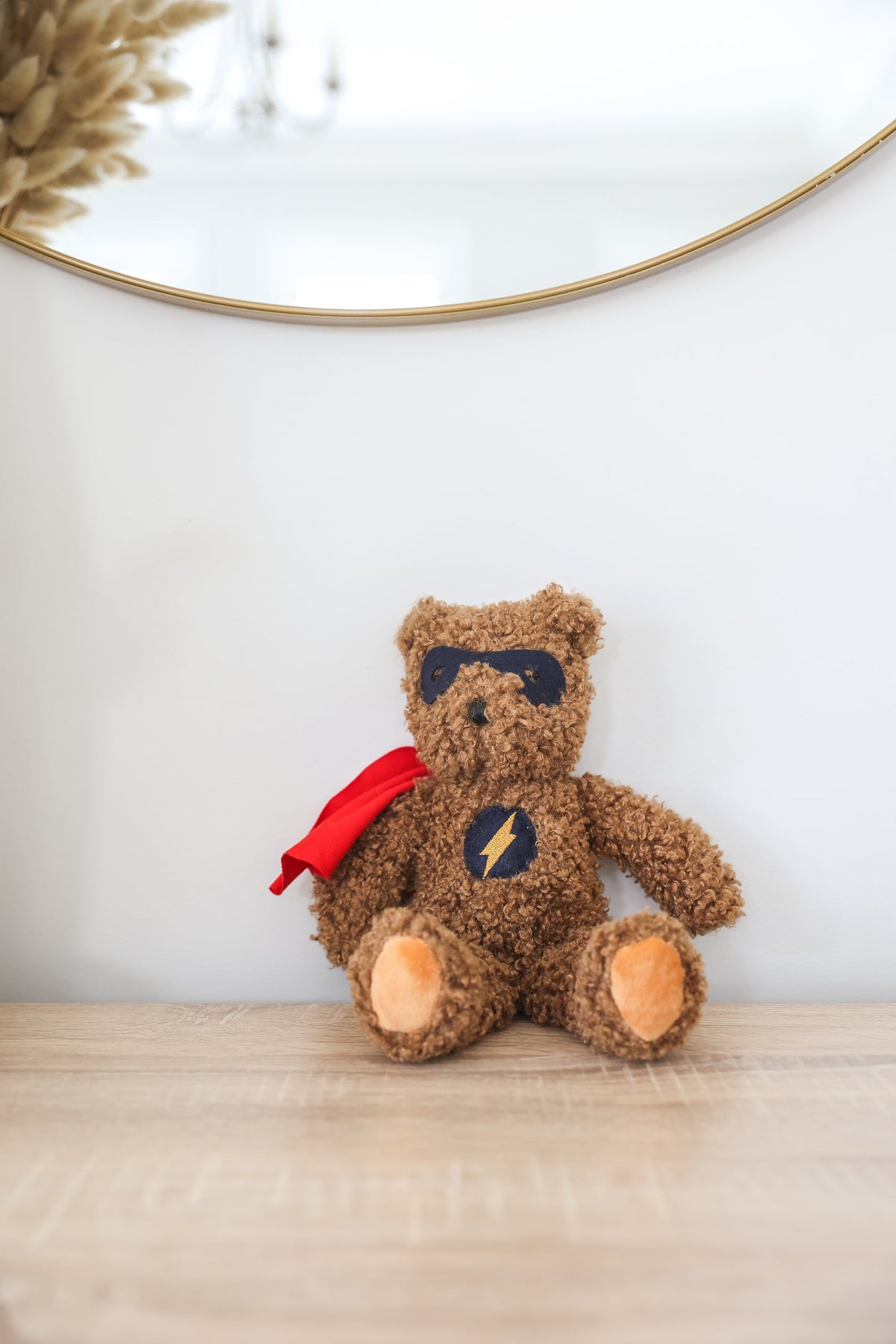 Teddy bear with a superhero cape on a wooden surface with a white wall background