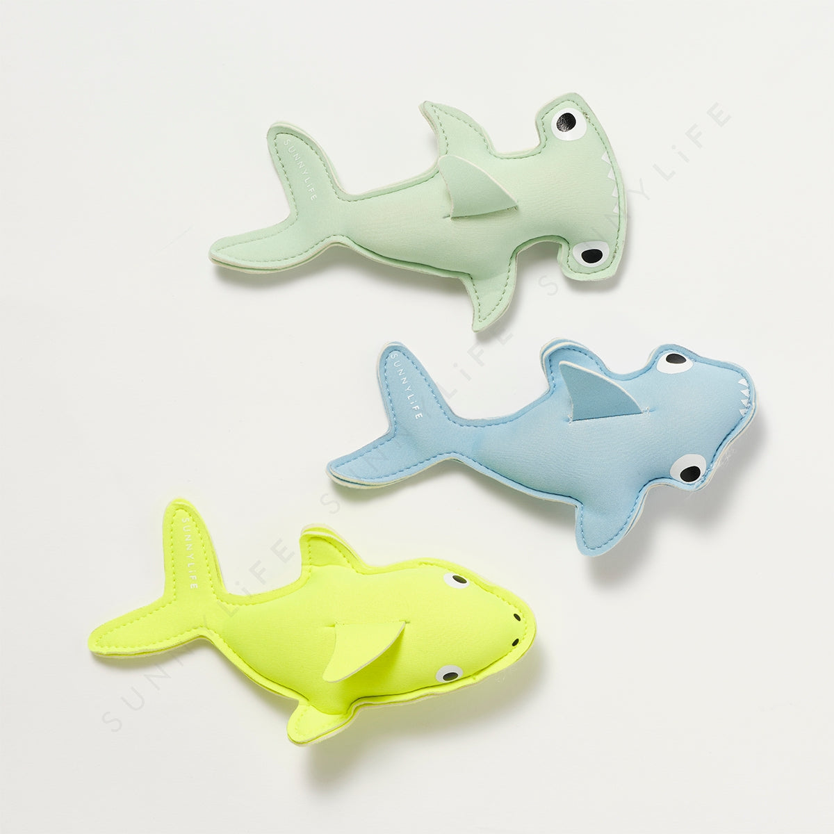 Three shark-shaped bath toys in green, blue, and yellow on a white background