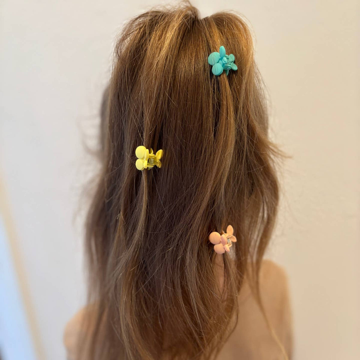 Person with long hair wearing colorful hair clips on a plain background