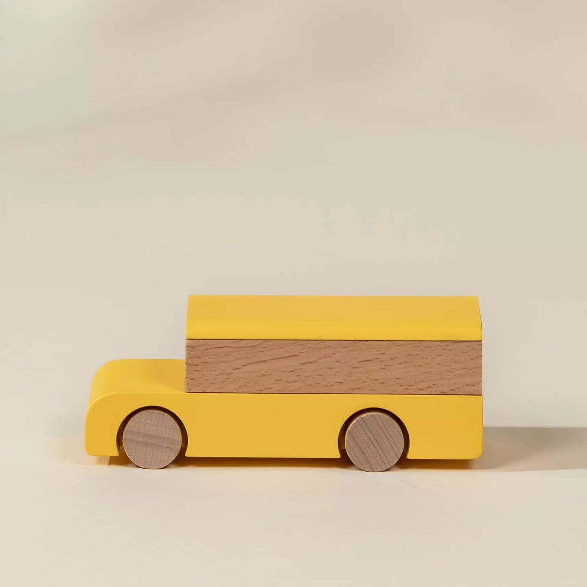 A wooden toy bus with a bright yellow body and a natural wood grain panel on the side, set against a plain light beige background.