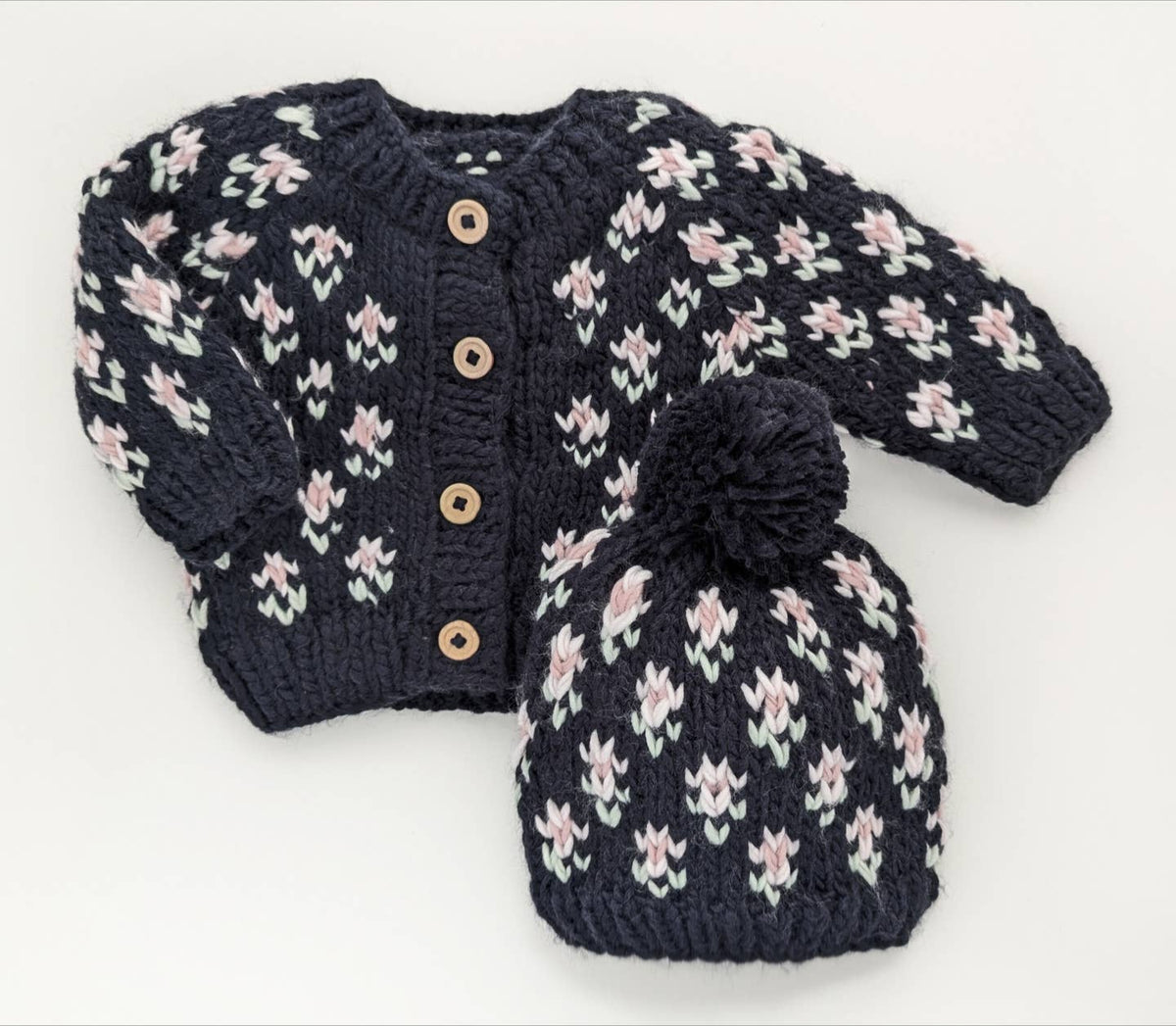 Knitted baby cardigan and hat set with floral pattern on a white background