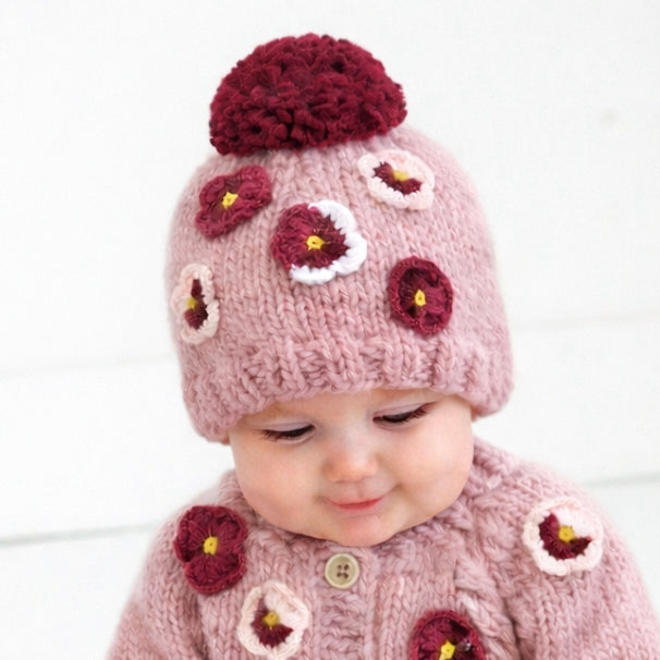 Baby wearing a pink knitted hat with floral patterns on a white background