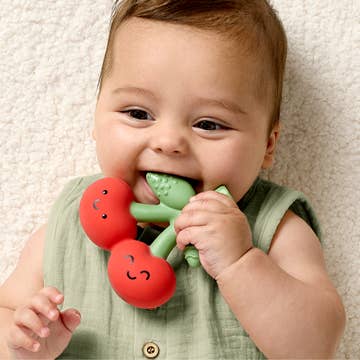 Baby chewing on a red and green teething toy against a neutral background