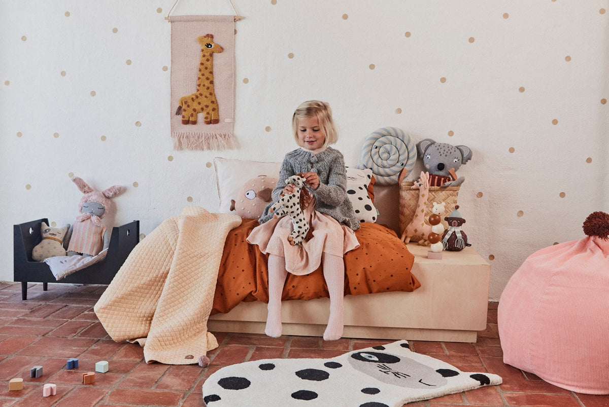 Child sitting on a bench in a playroom with toys and decorations.