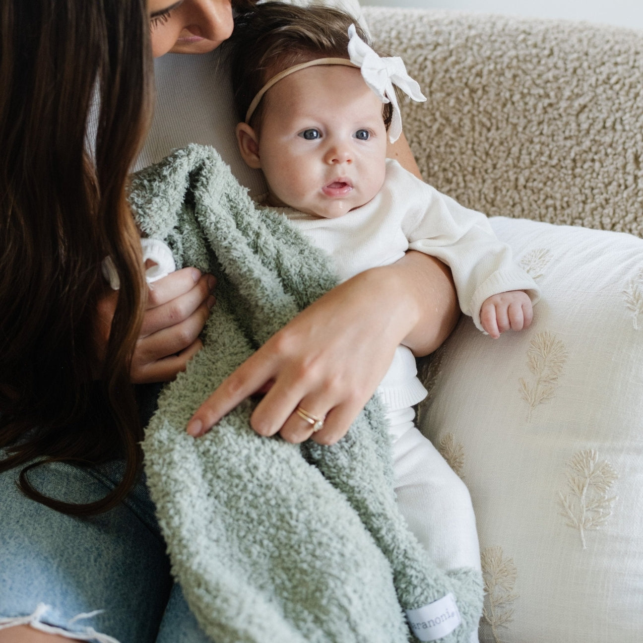 Woman holding a baby wrapped in a green blanket on a couch